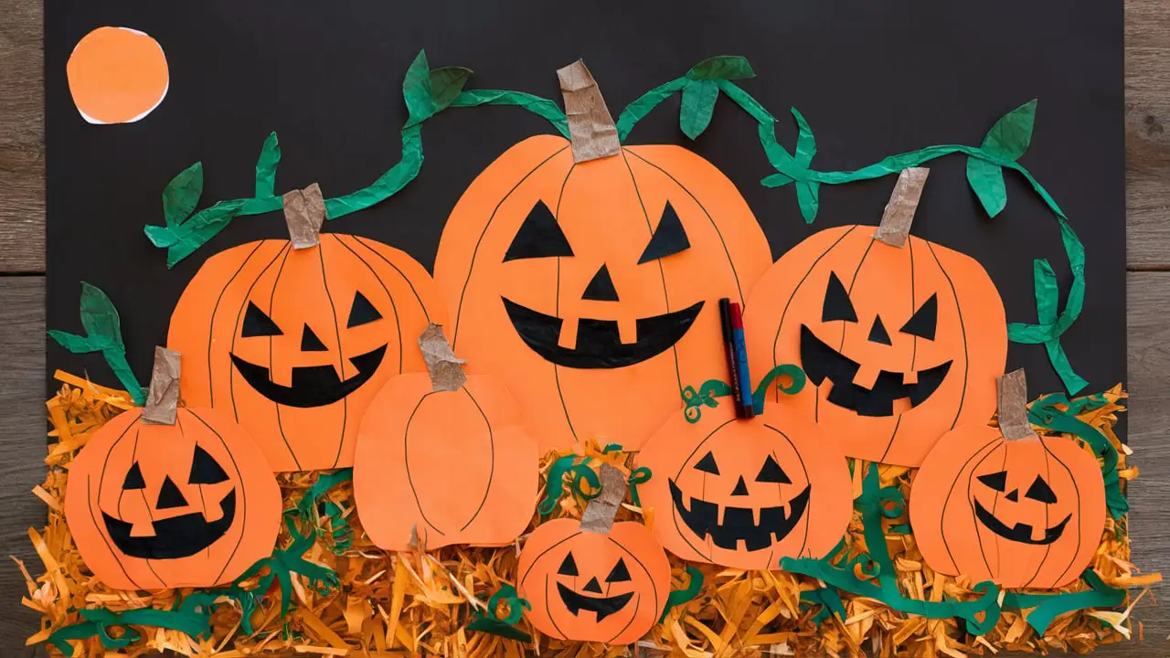 A vibrant pumpkin patch collage featuring several orange paper pumpkins with jack-o'-lantern faces, green vines, and stems on a black background. The pumpkins are surrounded by shredded yellow paper to resemble hay.